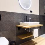 Badezimmer mit Waschbecken auf Holzkonsole, runden Spiegel und Dusche mit Glaswand.