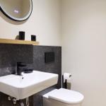 Badezimmer mit Waschbecken, Toilette und runden Spiegel.