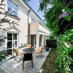 Terrasse mit Tisch und Stühlen, umgeben von grüner Vegetation und einem Holzzaun.