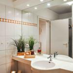 Badezimmer mit Waschbecken, Spiegel und Dusche. Wandfliesen mit orangefarbenem Muster.