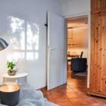 Schlafzimmer mit Blick in Wohnbereich. Holzschrank, Nachttisch und Stehlampe.