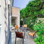 Terrasse mit Tisch und vier Stühlen, umgeben von grünen Pflanzen und einer Steinmauer.