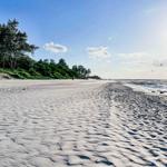 Weiterer Sandstrand mit Bäumen und Kitesurfern am Horizont.
