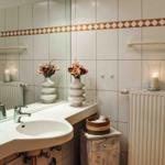 Badezimmer mit Waschbecken, Spiegel, Heizkörper und Vasen mit Blumen.