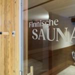 Finnische Sauna mit Holzbank und Glaswand. Tür mit Holzverkleidung und Aufschrift.