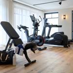 Fitnessraum mit Laufband, Crosstrainer und Bank. Holzboden und große Fenster.