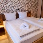 Doppelbett mit weißen Laken und Handtüchern, Wand mit Muschel-Motiv und Holzkopfteil.