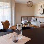 Esstisch mit Wasserglas und Karaffe im Essbereich. Im Hintergrund Sofa und Fenster.