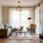 Wohnzimmer mit Sofa, Sessel und Tisch vor Fenster mit Vorhängen.