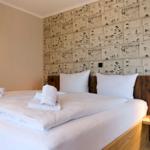 Ein Bett mit weißer Bettwäsche und Handtüchern. Wand mit Zeichnungen und Holzkopfteil.