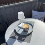 Runder Tisch mit Laterne und Tasse auf Balkon. Hintergrund: Sitzgelegenheit mit Kissen.