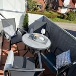 Terrasse mit Tisch und drei Stühlen, Pflanze und Blick auf Wohnhäuser.