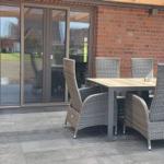 Terrace with dining table, chairs, and grill. Background: red brick wall and glass doors.
