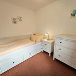 Bedroom with white bed, nightstand, and dresser. Wall art and carpeted floor.