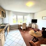 Kitchen with dining area and living room with sofa, TV, and windows.