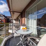 Terrasse mit Tisch, Stühlen und Korb mit Orangen. Blick auf Wohnhäuser und Himmel.