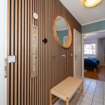 Eingangsbereich mit Holzwand, runder Spiegel und Sitzbank. Blick in Schlafzimmer mit Bett.