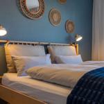 Ein Bett mit weißer Bettwäsche und blauer Decke vor blauer Wand mit Wanddekoration.