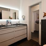 Badezimmer mit Doppelwaschbecken, beleuchtetem Spiegel und Holzdekoration.