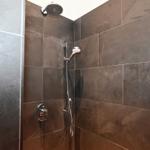 Dusche mit dunklen Fliesen und Duschkopf