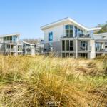Modern vacation homes with balconies stand behind tall grass.