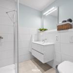 Moderne Badezimmer mit Dusche, Waschbecken und Toilette. Weiße Fliesen und Spiegelschrank.