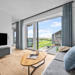 Wohnzimmer mit Sofa, TV und großem Fenster mit Blick auf Grünfläche.