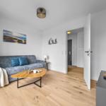 Wohnzimmer mit Sofa, Couchtisch und Fernseher. Holzboden und Wandbild mit Strandmotiv.