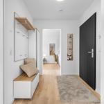 Hausflur mit Holzboden, Wandgarderobe und Teppich. Tür und Wohnzimmer sichtbar.