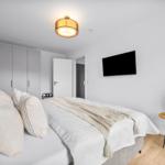 Schlafzimmer mit Bett, Kleiderschrank, Fernseher und Pflanze auf Tisch.