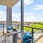 Terrasse mit Tisch, Stühlen und blauen Kissen. Blick auf grüne Landschaft und Häuser.