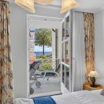Zimmer mit Blick auf Balkon und Meer. Vorhänge, Bett und Lampe sichtbar.