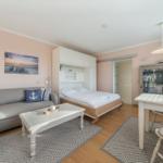 Living area with sofa, bed, and dining table. Wall art shows beach.
