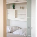 Bedroom with white bed and integrated cabinet with shelf and plant.