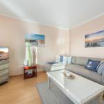 Living room with sofa, coffee table, and TV. Wall art shows beach landscapes.