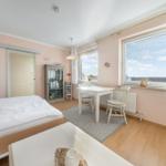 Bedroom with bed, desk, and windows. Wooden floor and pink walls.
