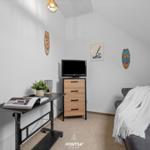 Schlafzimmer mit TV, Schreibtisch und Sofa unter Dachschrägen.