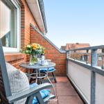 Balkon mit Tisch, Stühlen und Blumenarrangement. Blick auf Wohnhäuser und Himmel.
