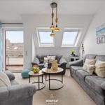Wohnzimmer mit grauen Sofas, runden Tischen und Dachfenstern. Balkon und Wandbilder sichtbar.