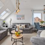 Wohnbereich mit grauen Sofas, Esstisch und Dachfenstern. Wandbild und Hängelampen.