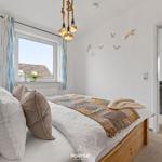 Schlafzimmer mit Bett, Fenster und Wanddekoration. Durchgang zum Wohnbereich.