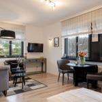 Living space with sofa, TV, dining table, and bed. Windows with blinds and view of garden.