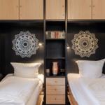 Two beds with white bedding, black walls with mandala motifs and wooden shelves.