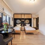 Two beds, table with chairs, window view. Wooden floor and cabinets.