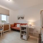 Wohnküche mit Sofa, Tisch und Fenster. Küchenzeile mit Spüle und Arbeitsfläche.