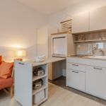 Küche mit Arbeitsfläche, Spüle und Kühlung. Nebenraum mit Sofa und Lampe.