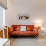Ein Raum mit orangefarbenem Sofa, weißen Möbeln und einem Fenster mit Jalousie.