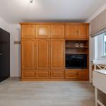 Großer Schrank mit TV-Nische, Fenster mit Blumen, weiße Tischplatte und Holzboden.