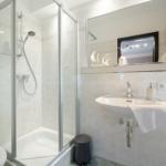 Badezimmer mit Dusche, Waschbecken und Spiegel. Weiße Fliesen und Handtuchhalter.
