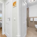 Badezimmer mit Dusche, Toilette und Handtuchständer. Durchgang zu Schlafzimmer mit Bett und Fenster.